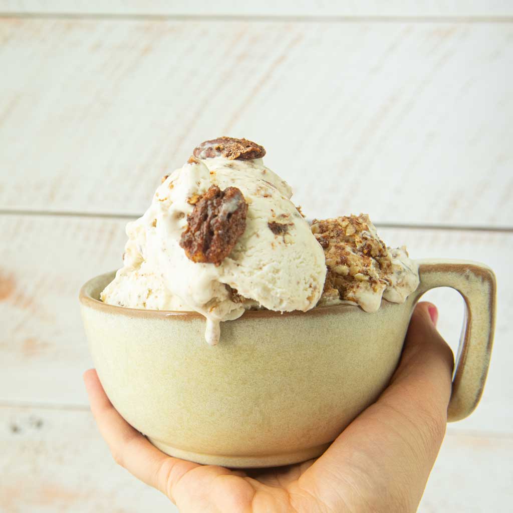 hand holding cup of candied pecan ice cream with whole candied pecans
