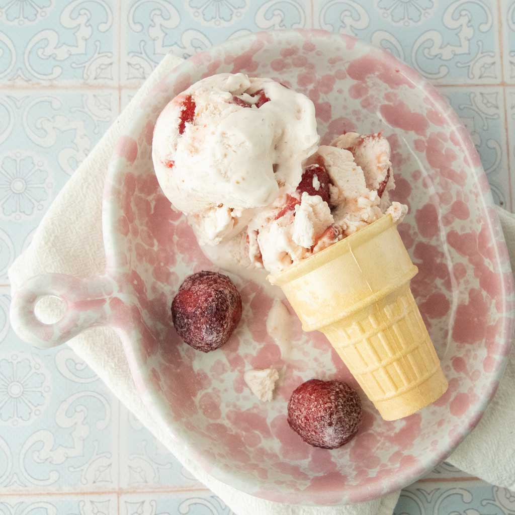 cone of strawberry cheesecake ice cream and whole strawberries in pink and white dish