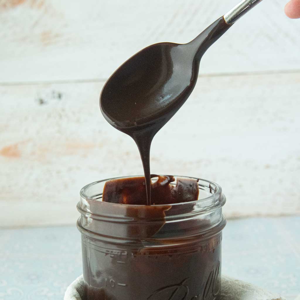 fudge sauce dripping into jar from spoon