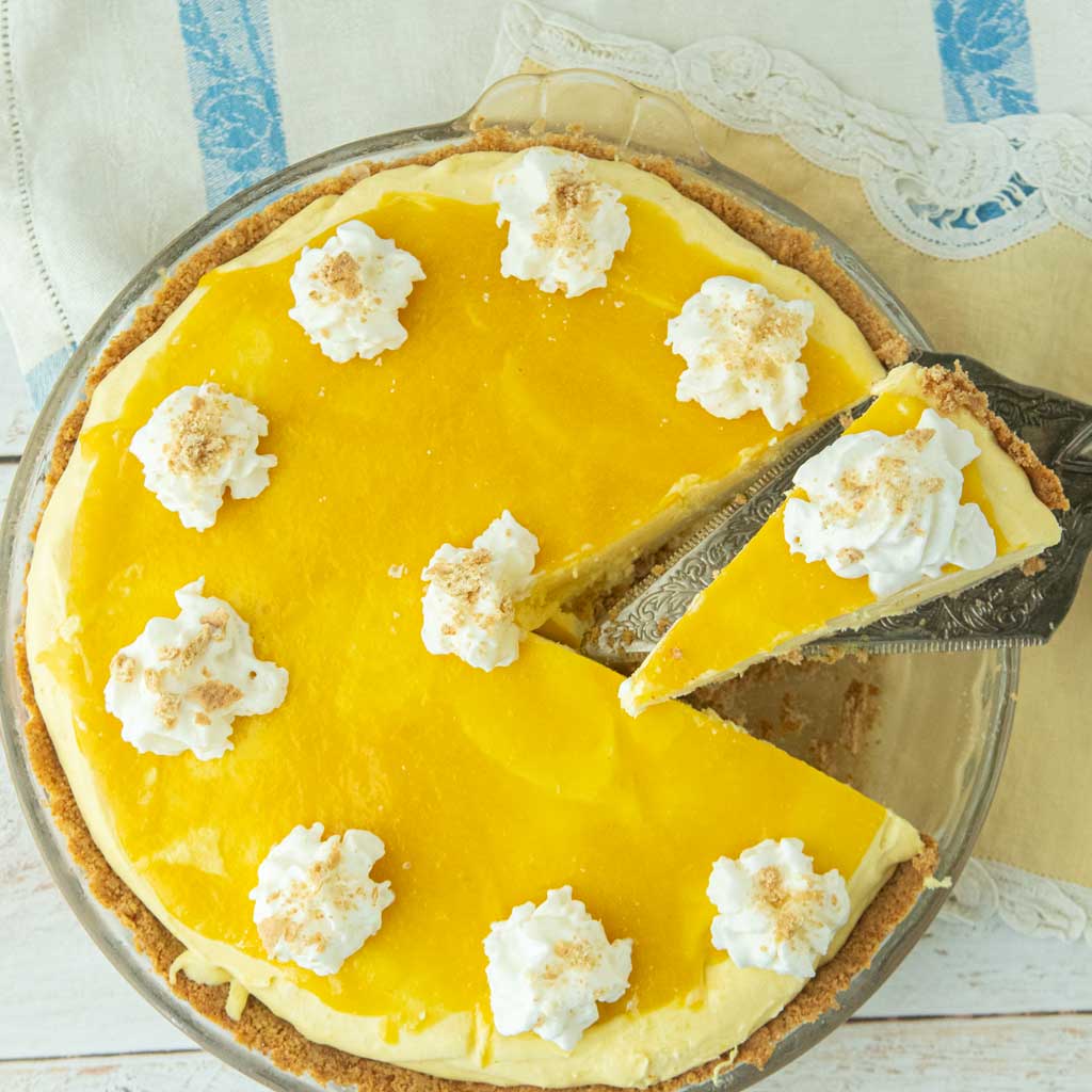 slice of mango pie cu out of whole pie topped with whipped cream on pie server