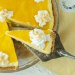 slice of mango pie cu out of whole pie topped with whipped cream on pie server