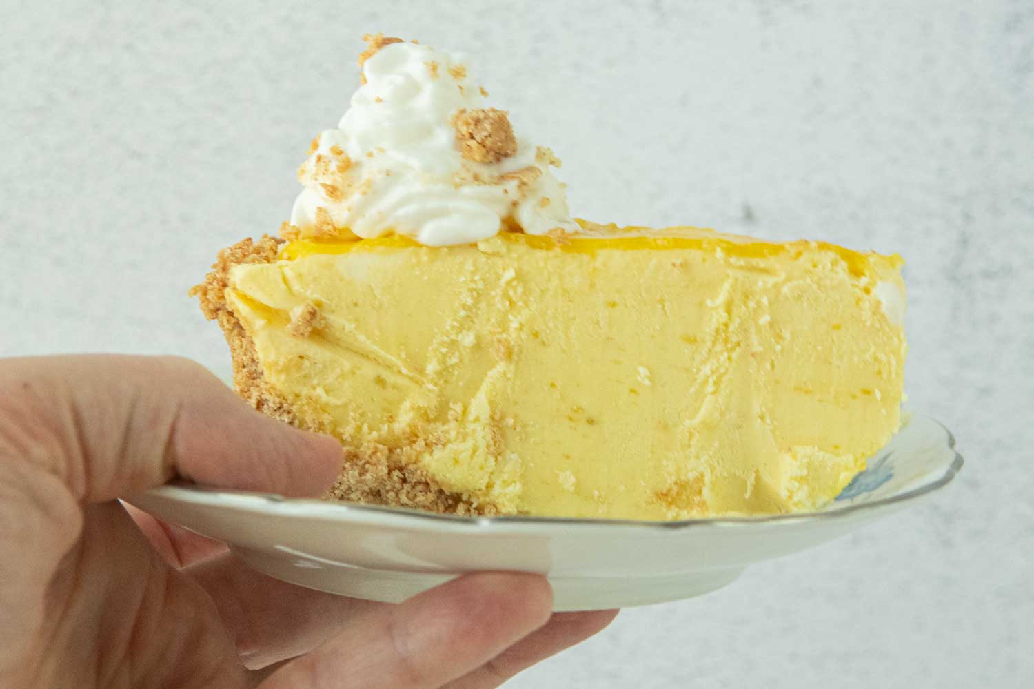 hand holding slice of mango pie on plate topped with whipped cream