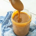 dulce de leche falling off spoon into jar of dulce de leche on top of blue napkin