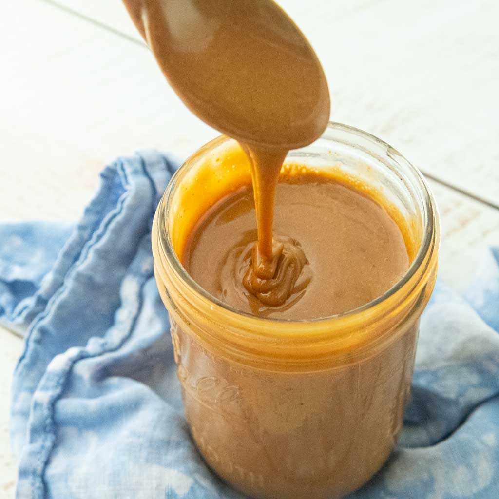 dulce de leche falling off spoon into jar of dulce de leche on top of blue napkin