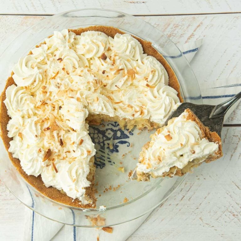 coconut cream pie with slices cut from it and slice on pie server