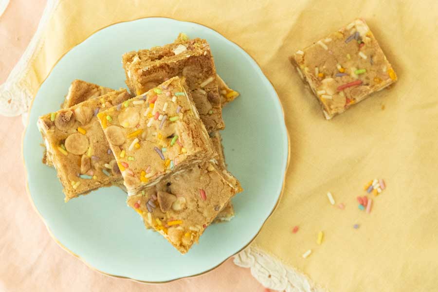 cut birthday cake blondies on plate, single blondie on napkin and sprinkles