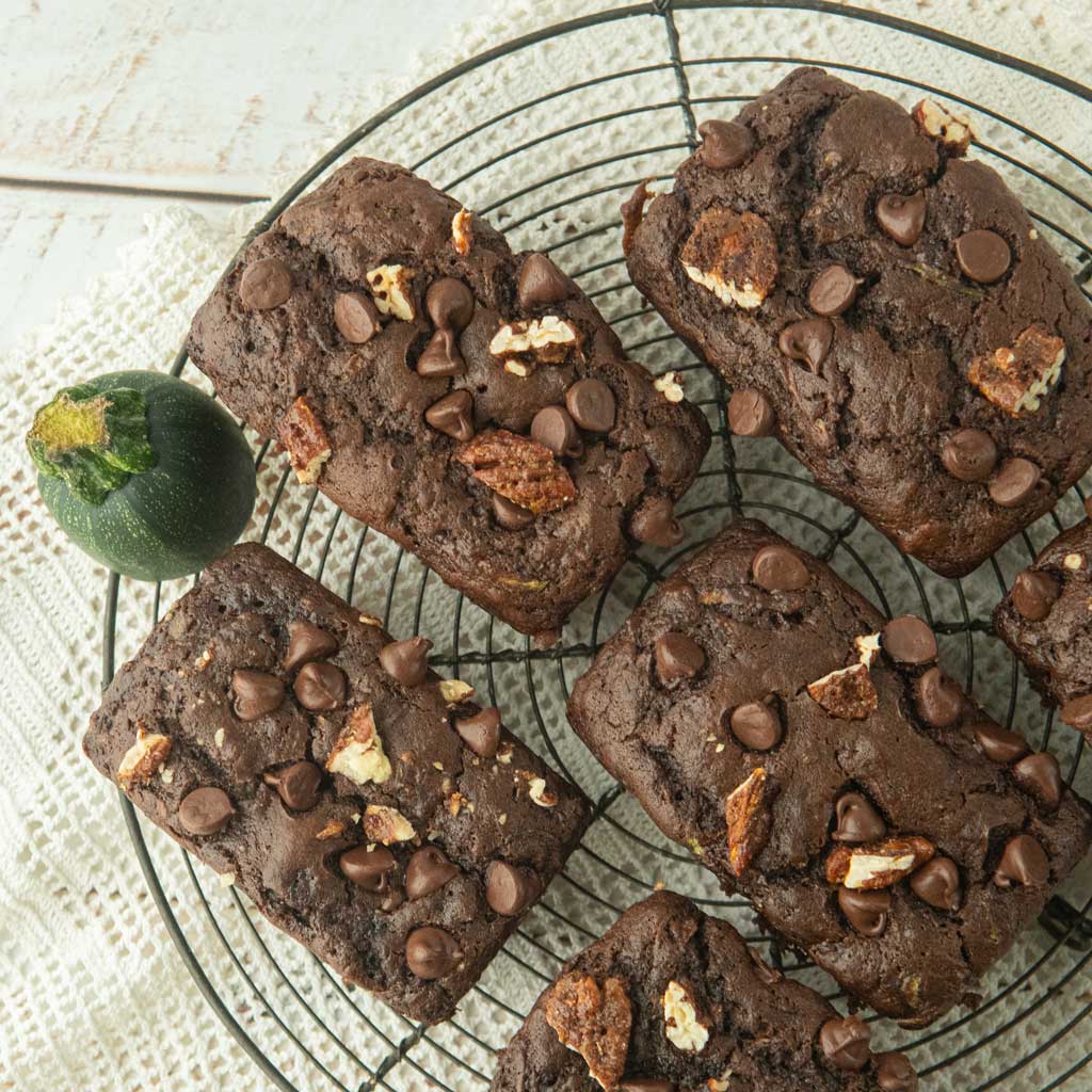 mini loaves of chocolate zucchini bread on wire rack, piece of zucchini