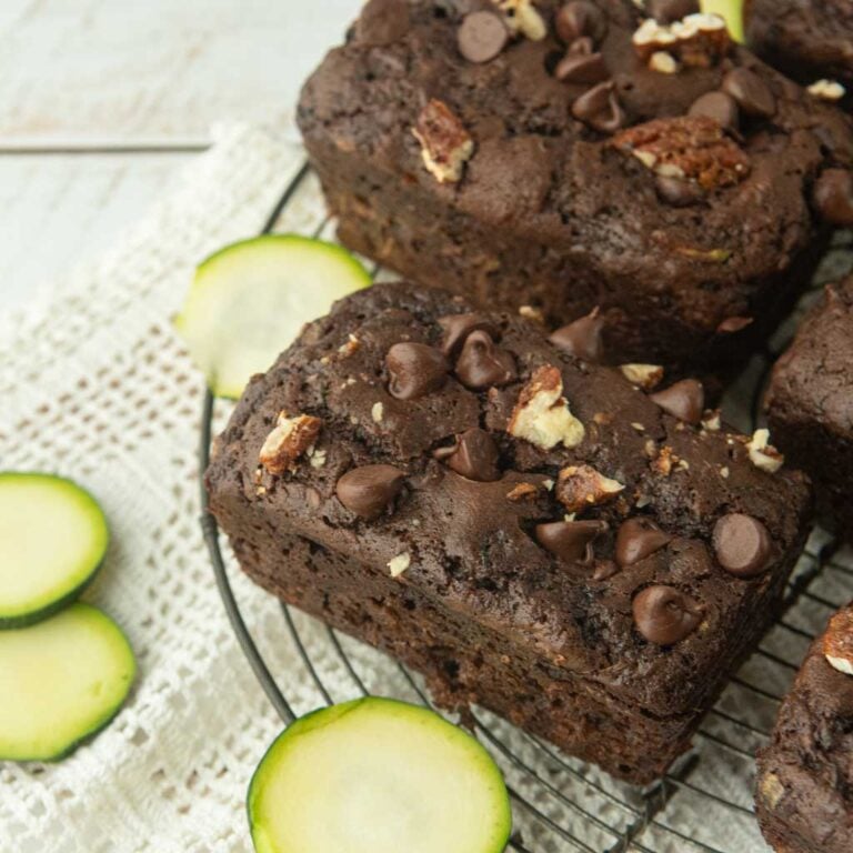 slices of zucchini next to small loaves of chocolate zucchini bread topped with chocolate chips and chopped pecans