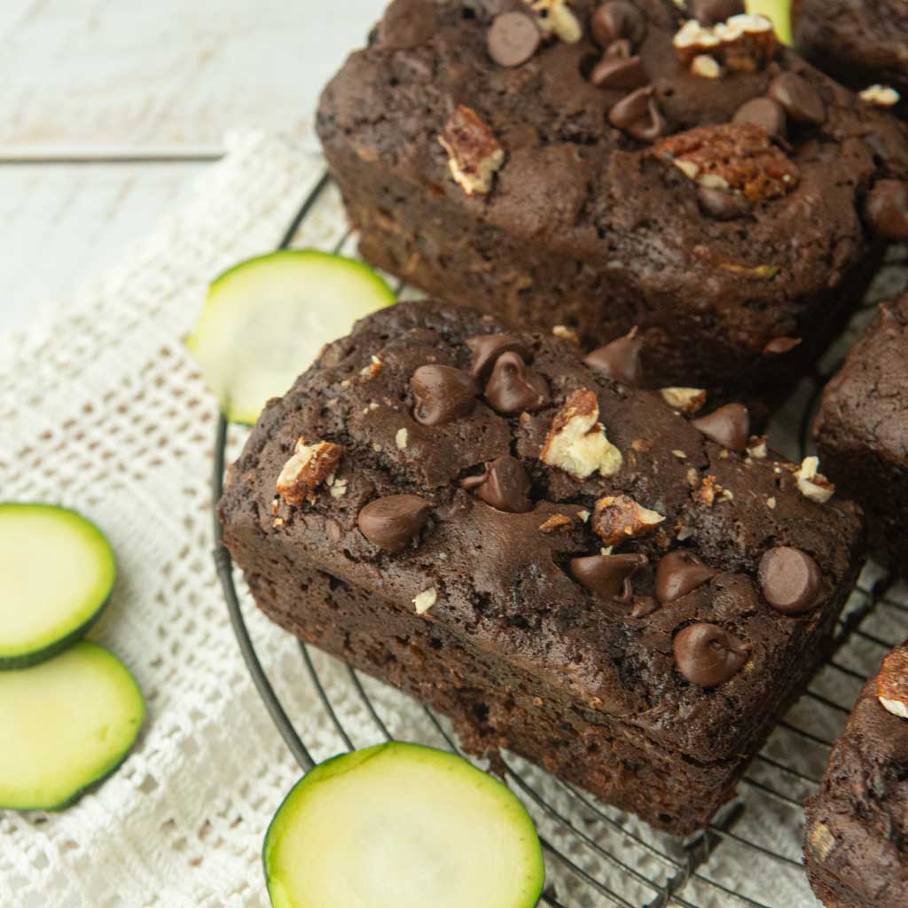 slices of zucchini next to small loaves of chocolate zucchini bread topped with chocolate chips and chopped pecans