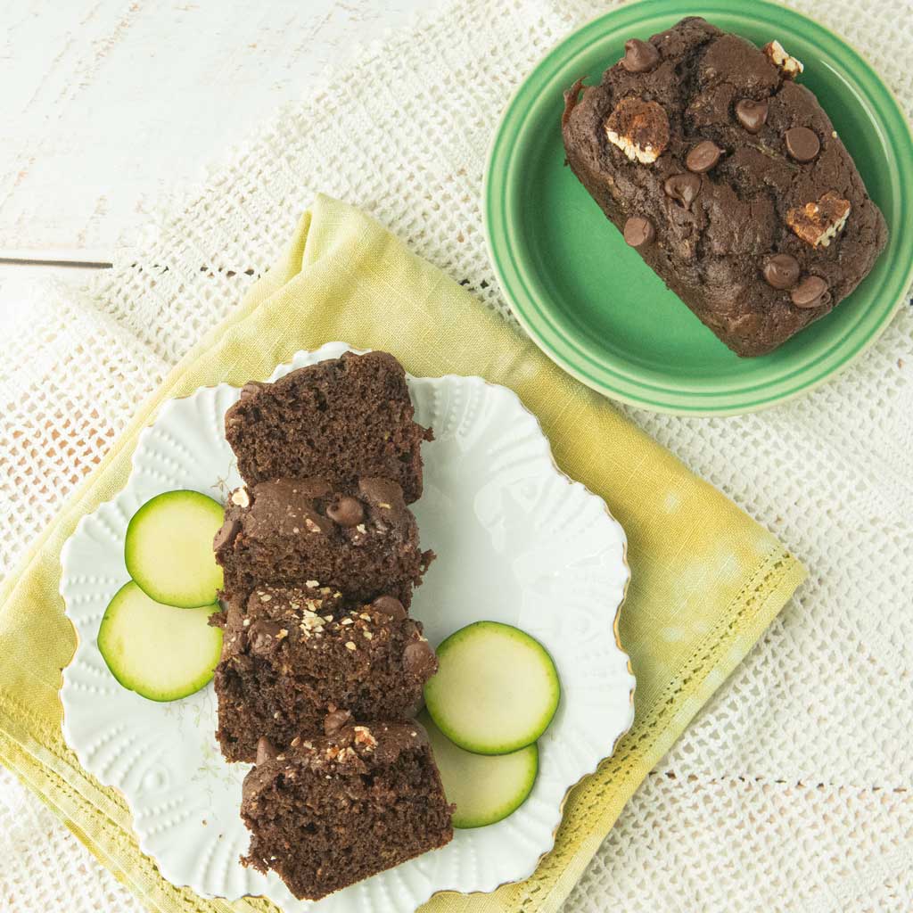 slices of chocolate zucchini bread on plate with zucchini slices, green plate with loaf of chocolate zucchini bread