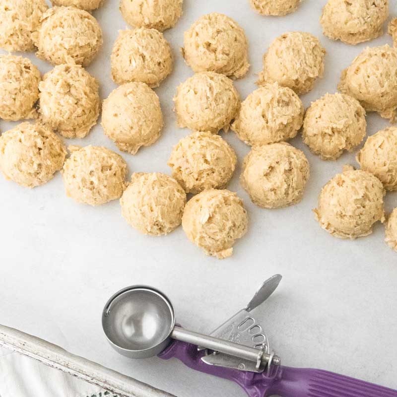 oatmeal cookie dough scoops on sheet tray next to cookie scoop