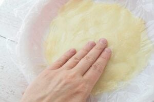 hand pressing piece of plastic on top of pudding in pie plate