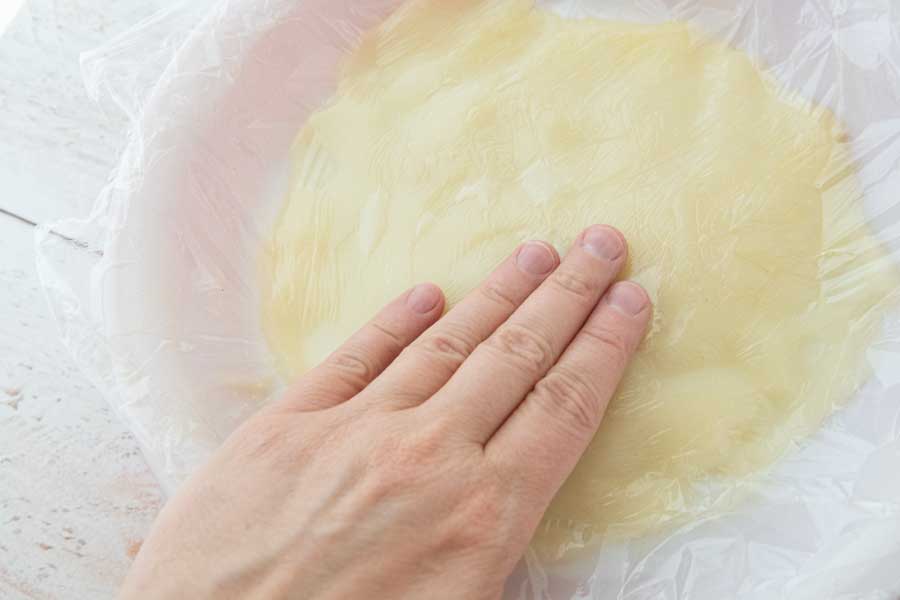 hand pressing piece of plastic on top of pudding in pie plate