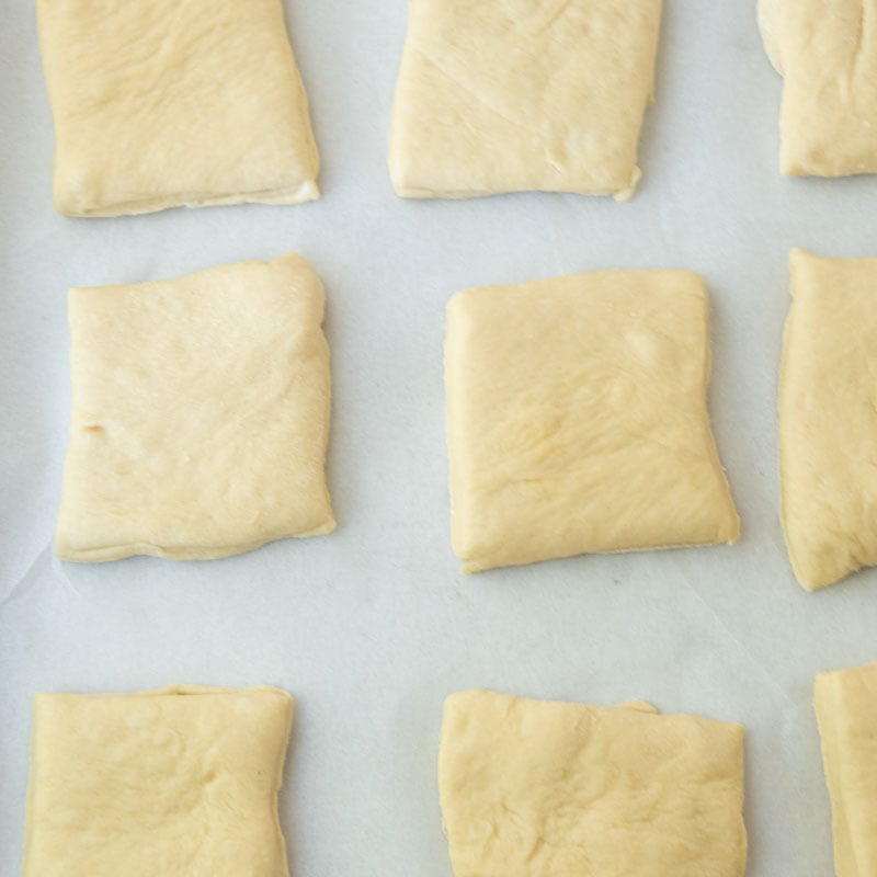 dough for homemade texas roadhouse rolls cut into squares on parchment
