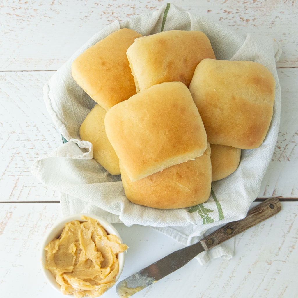 homemade texas roadhouse rolls in basket next to flat spatula and bowl of cinnamon honey butter