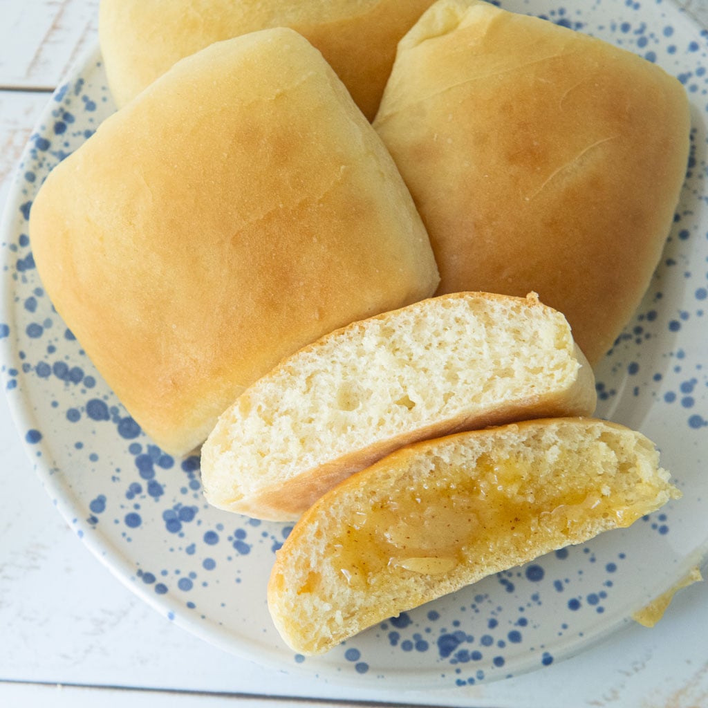 closeup of homemade texas roadhouse rolls, one cut open to show texture, one spread with cinnamon honey butter