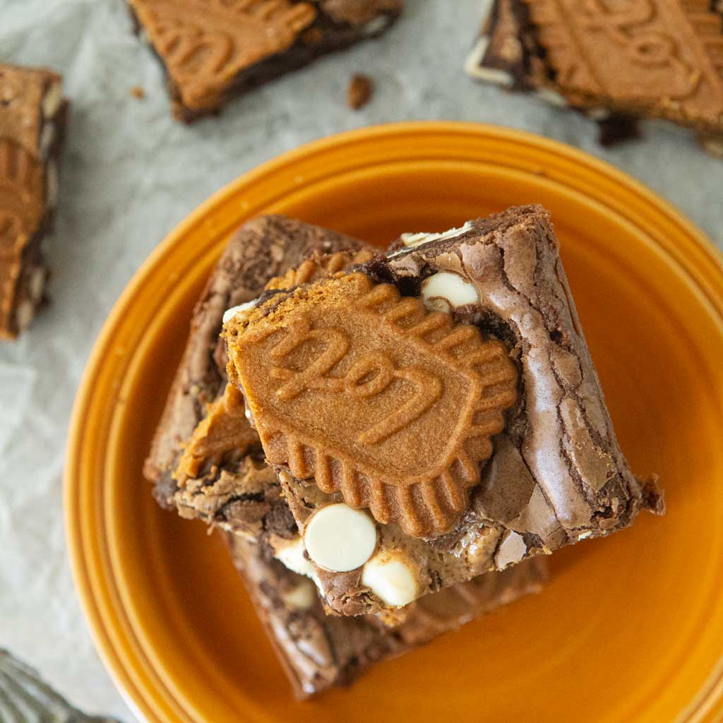 biscoff brownies stacked on orange plate next to whole biscoff brownies