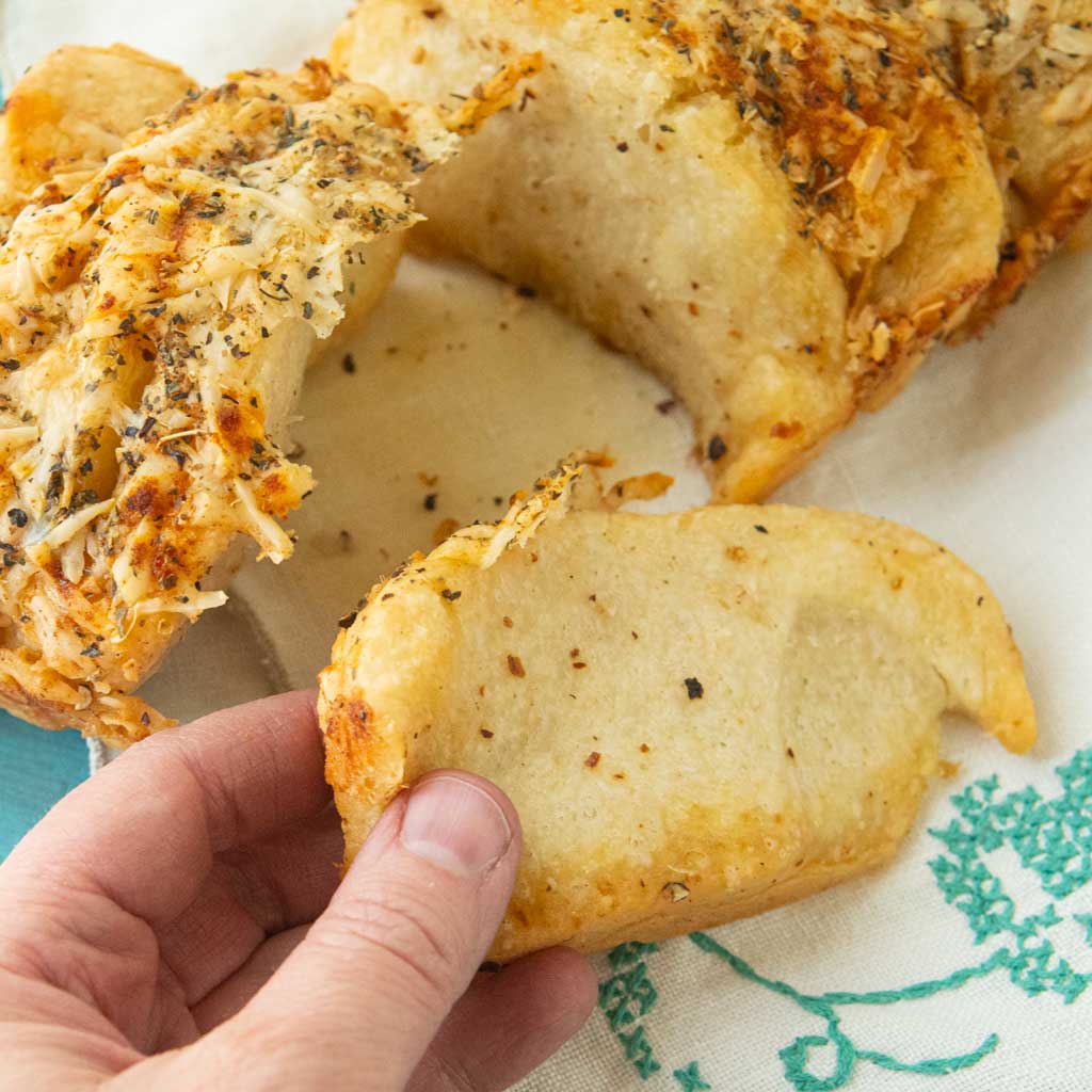 hand holding piece of pull apart garlic bread next to loaf of homemade pull apart garlic bread