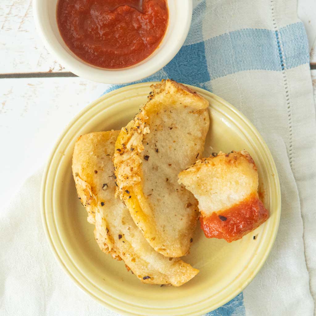 pieces of pull apart garlic bread next to cup of tomato sauce with one of the pieces dipped in sauce