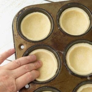 pressing rounds of cream cheese pastry into muffin tin for pie crusts