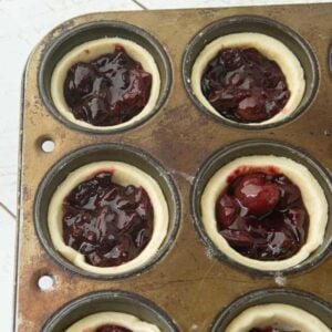 filling pie crusts in muffin tin with cherry filling