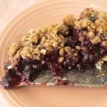 cherry crumble pie on pie server on pink plate