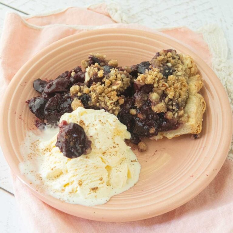 slice of cherry crumble pie on pink plate with vanilla ice cream topped with a cherry