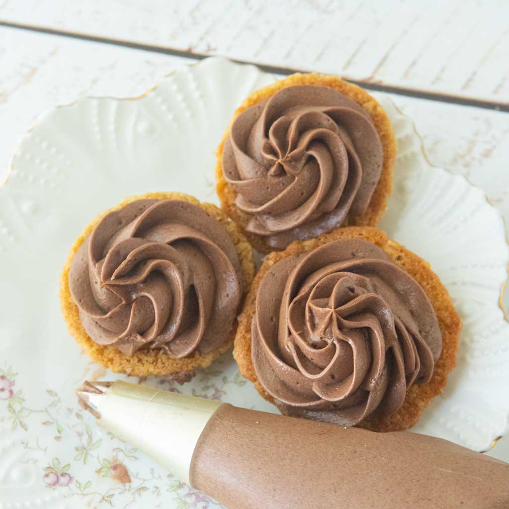 swirls of chocolate ermine frosting on backs of pumpkin oatmeal cookies, piping bag filled with chocolate ermine frosting