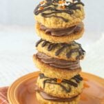 stack of pumpkin oatmeal cream pies covered with chocolate drizzle and sprinkles, filled with chocolate ermine frosting