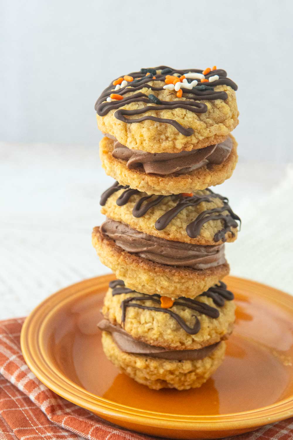 stack of pumpkin oatmeal cream pies covered with chocolate drizzle and sprinkles, filled with chocolate ermine frosting