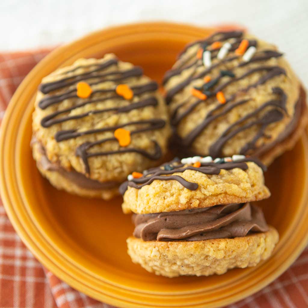 side and top views of chocolate ermine frosting filled pumpkin oatmeal cookies on orange plate