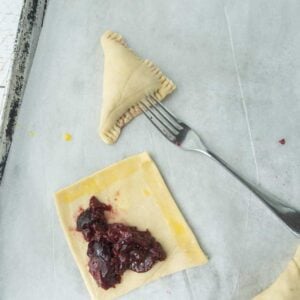 cherry turnover on baking sheet, fork, square of pastry and cherry filling