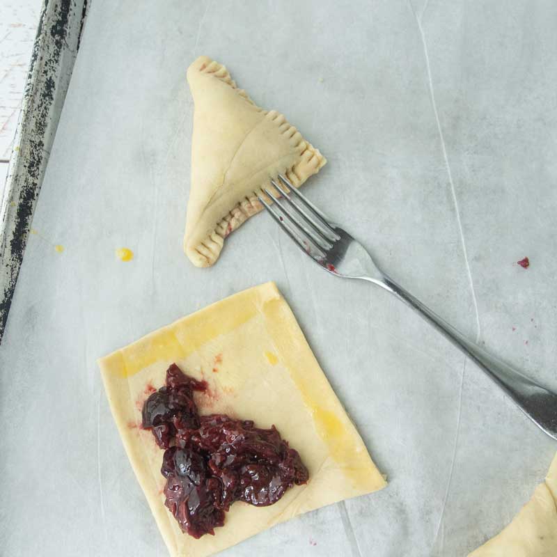 cherry turnover on baking sheet, fork, square of pastry and cherry filling
