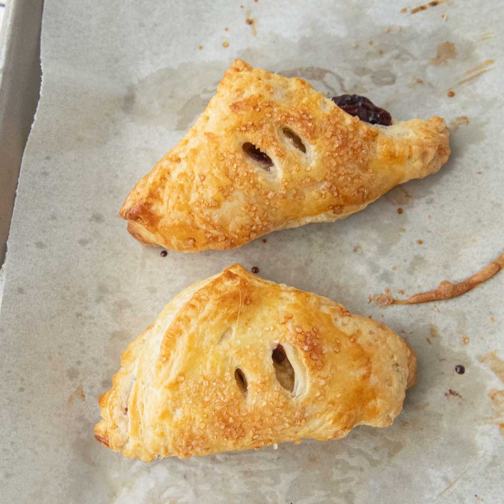 two baked cherry turnovers on parchment paper