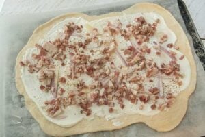 Flammkuchen dough topped with bacon and onions