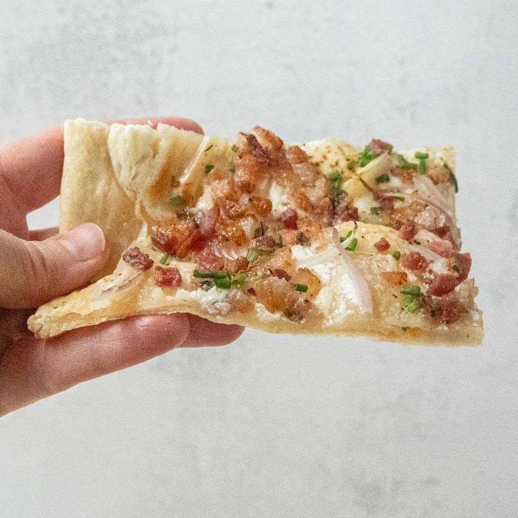 hand holding slice of flammkuchen