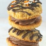 stack of pumpkin oatmeal cream pies covered with chocolate drizzle and sprinkles, filled with chocolate ermine frosting, text overlay