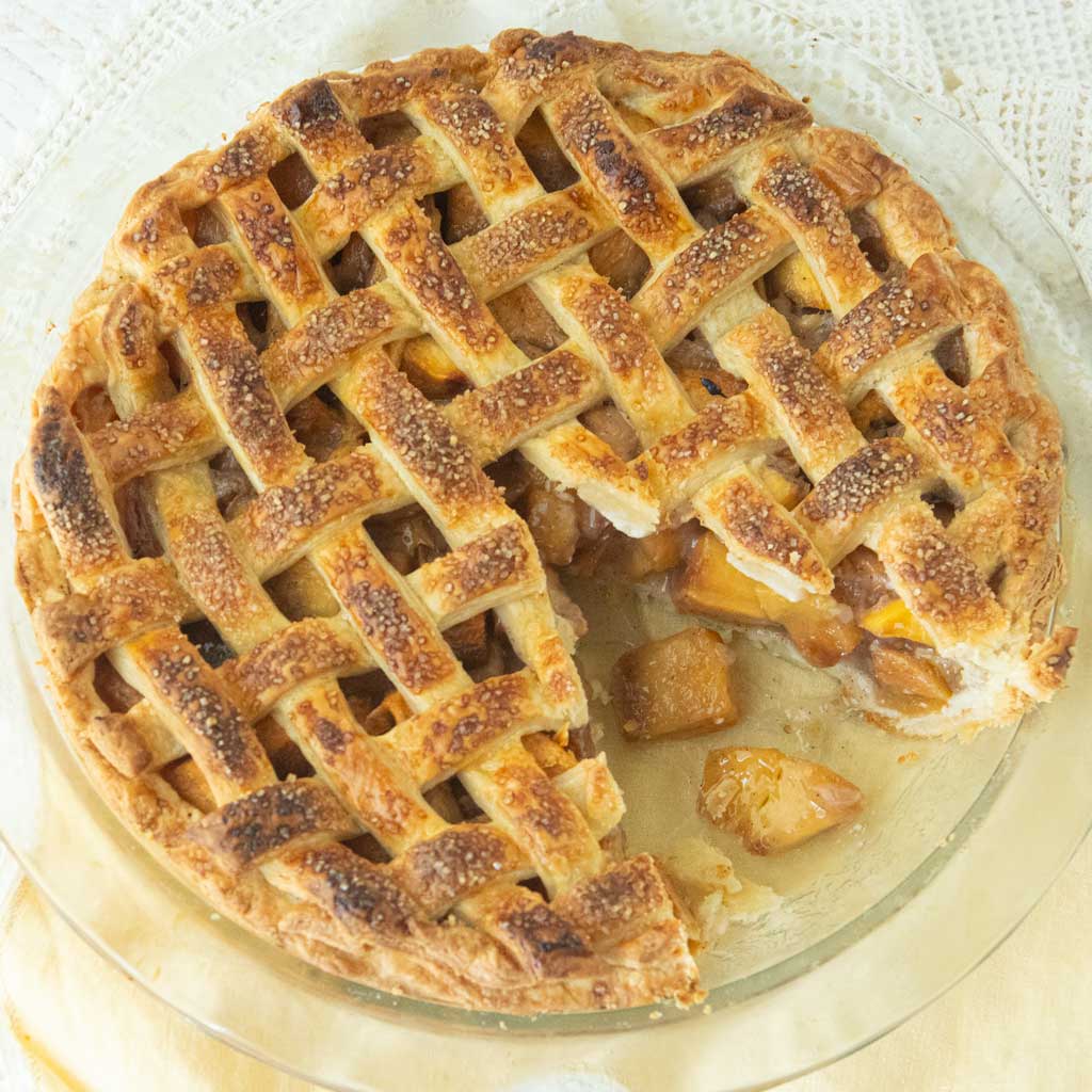 lattice top peach pie with slice cut from it