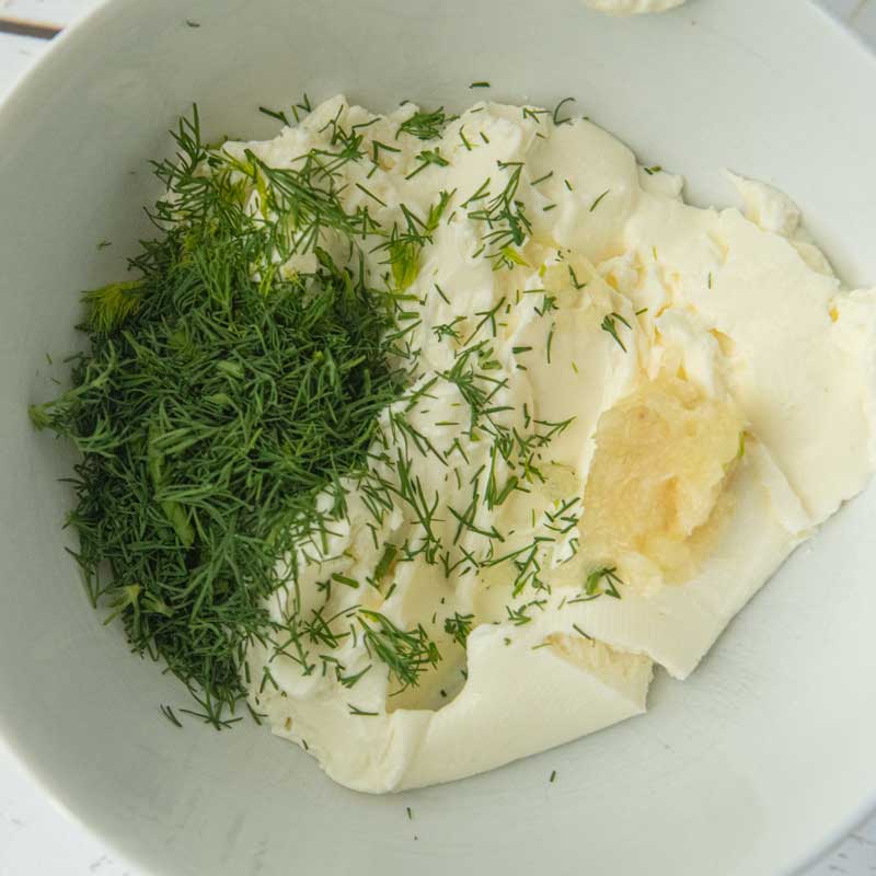 garlic and dill on top of cream cheese in bowl