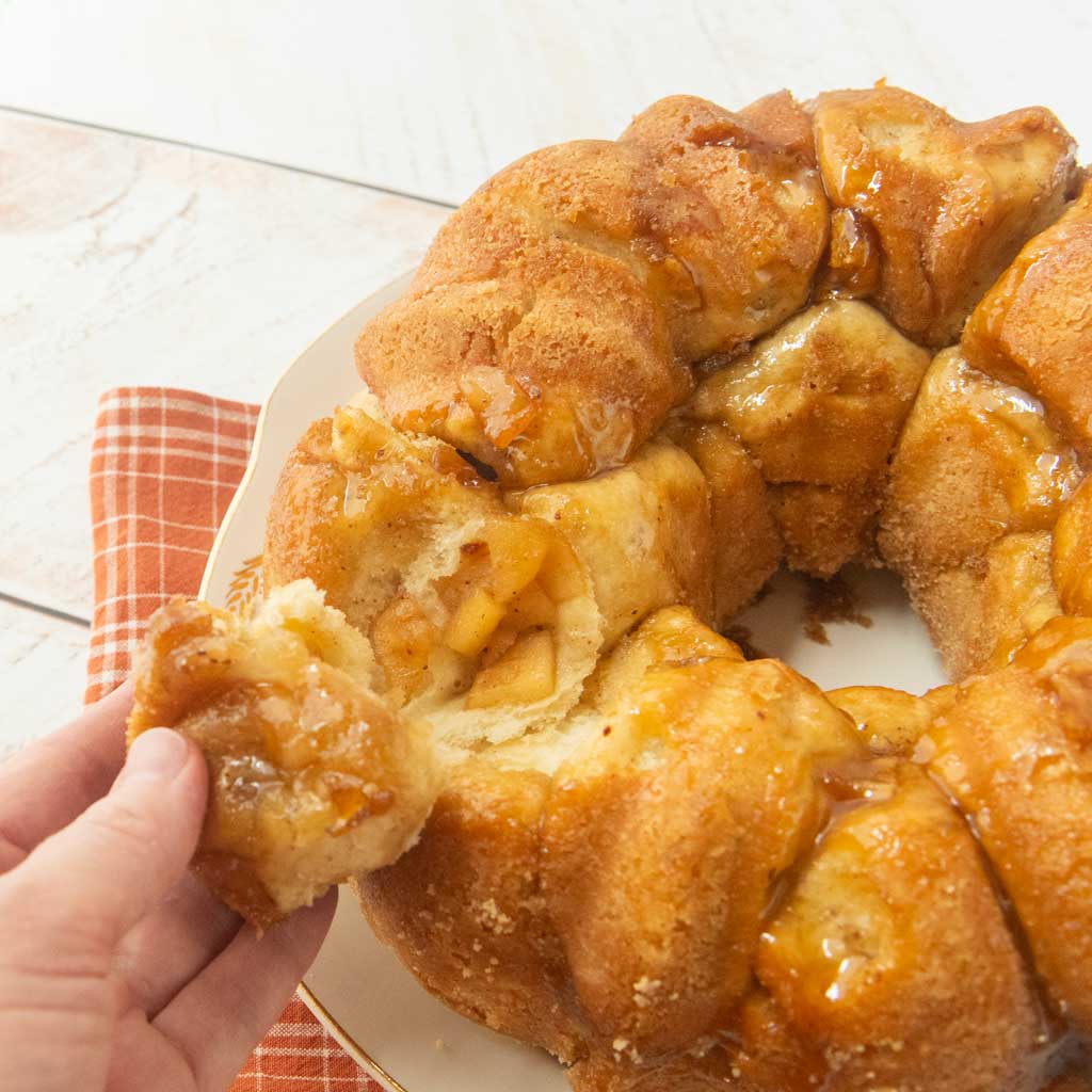 hand pulling away a piece of apple monkey bread next to plate of apple monkey bread