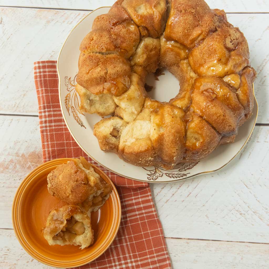 bundt pan ring of apple monkey bread on plate next to pieces of apple monkey bread on plate