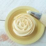 maple buttercream frosting on top of cupcake on plate next to piping bag of maple buttercream