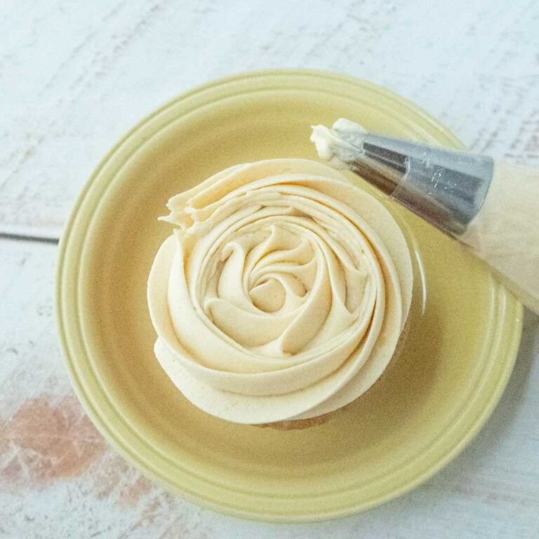 maple buttercream frosting on top of cupcake on plate next to piping bag of maple buttercream