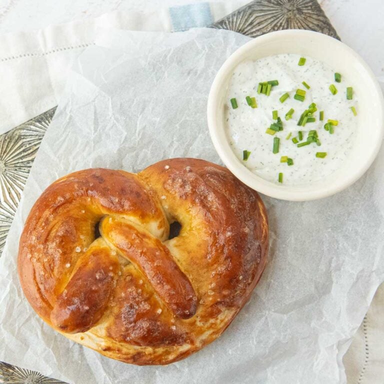 baked soft pretzel next to cup of chive dill whipped cottage cheese