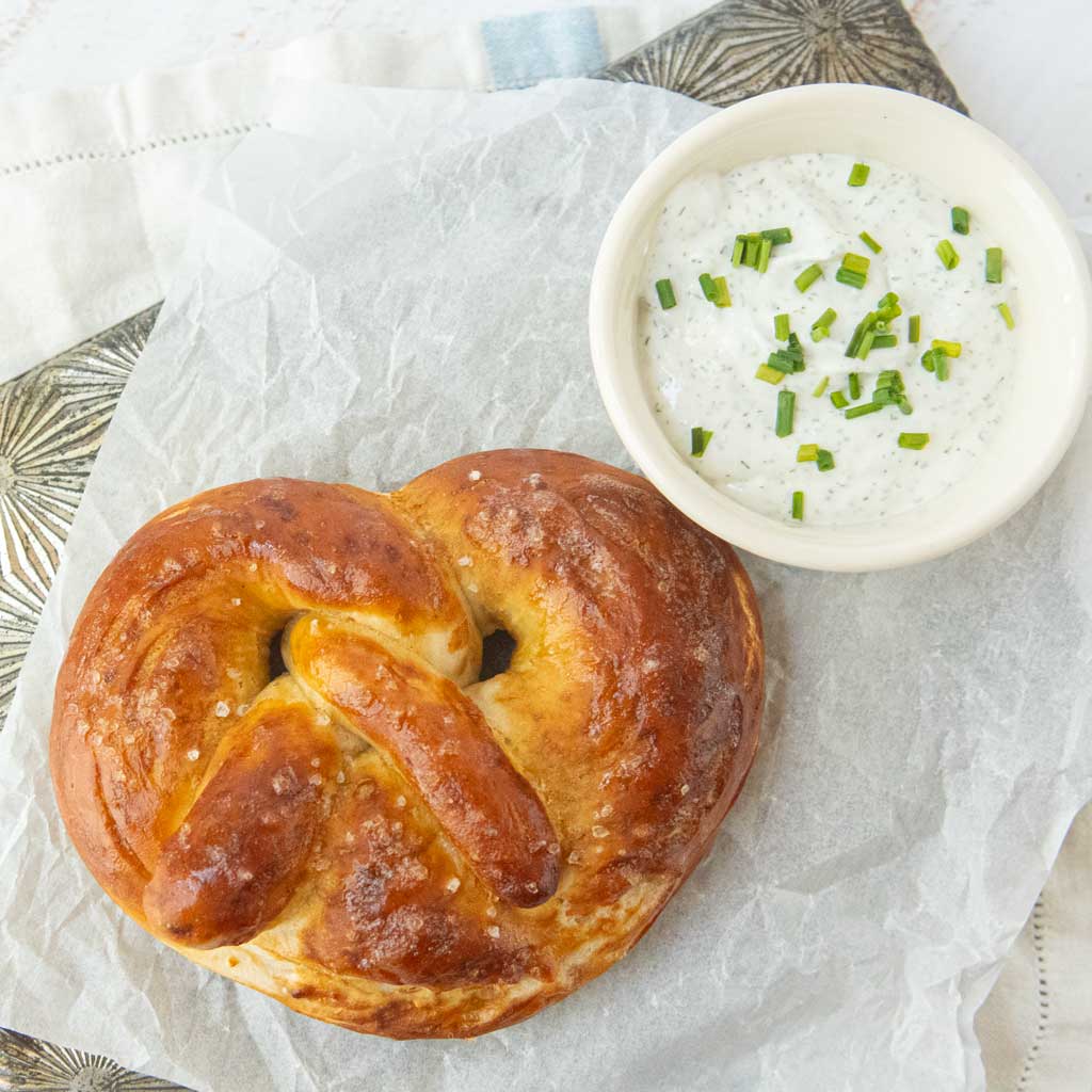 baked soft pretzel next to cup of chive dill whipped cottage cheese