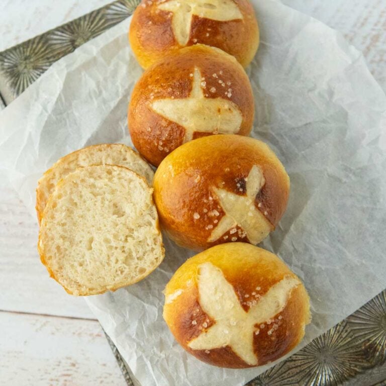 row of pretzel buns on paper next to spretzel bun split open to show texture