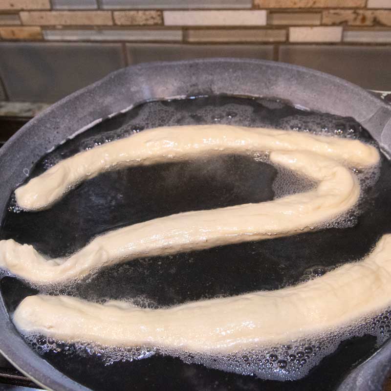 pretzel dough ropes in baking soda solution, boiling