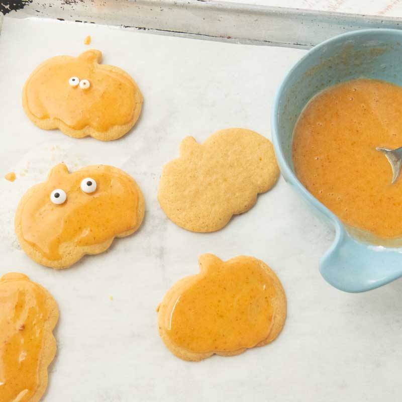 glazing pumpkin cutout cookies, adding candy eyes